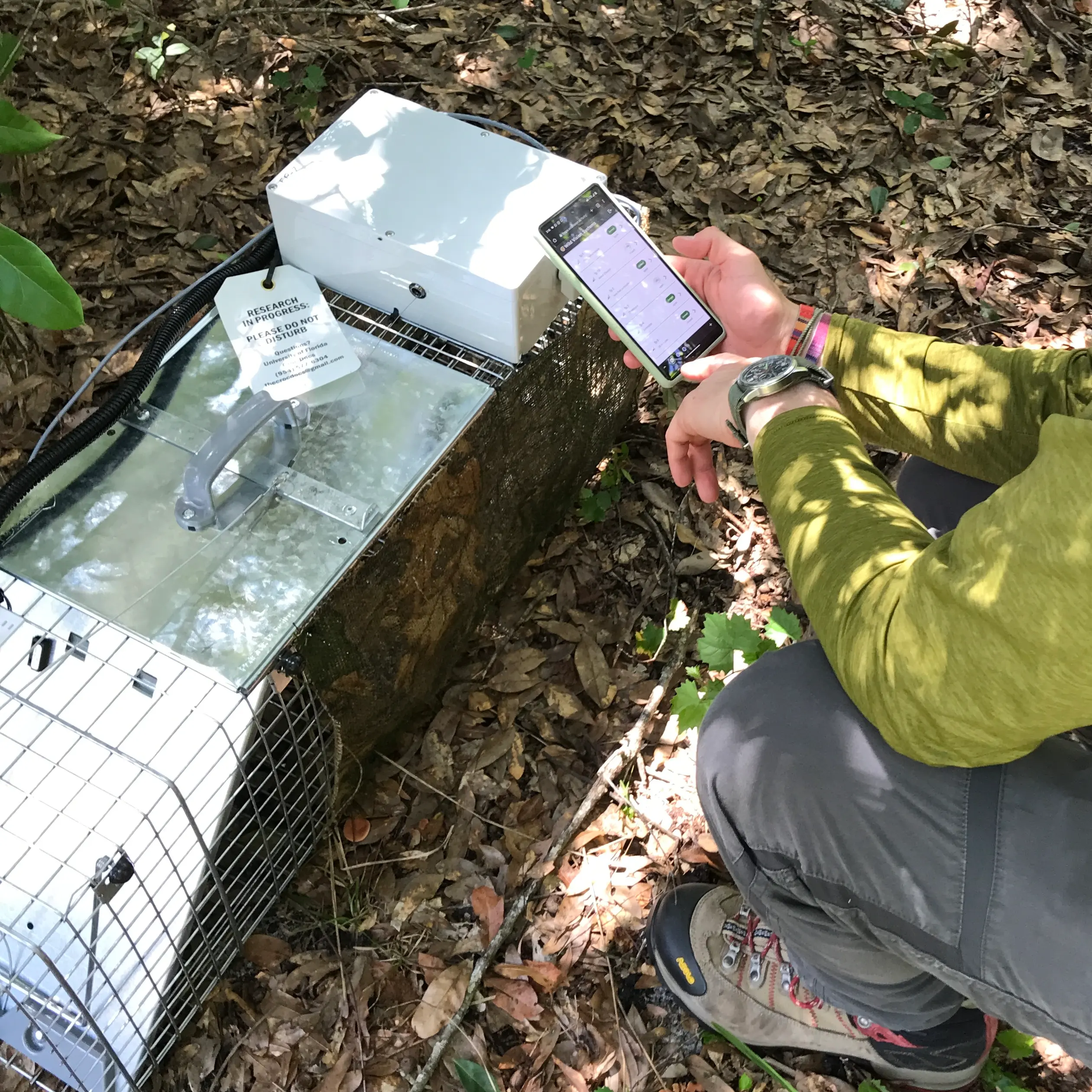 Photo of tech sitting by a smart trap and managing it using the app